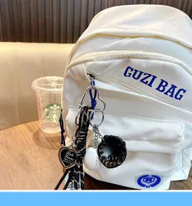 Close-up detail of a sports baseball charm and heart frame on a white backpack
