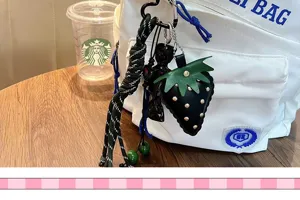 Detailed view of a leather strawberry keychain with green braided tassel hanging on a bag