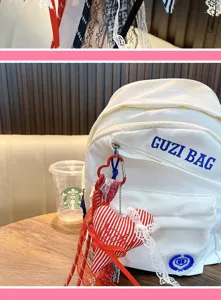 White backpack with red striped heart plush pendant, lace trim, and cute bag charm decor.