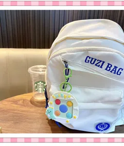 Detailansicht des weißen Rucksacks mit niedlichem Tier-Memory-Spiel-Schlüsselanhänger am Holztisch.