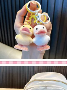 Detailed view of two cute yellow and white flocked duckling keychains held by hand