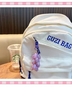Close-up detail showing the cute purple grape keychain hanging on the white backpack surface.