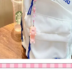 Detailed view of a cute pink pig keychain charm hanging on a white fabric backpack