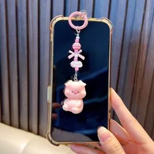 Cute pink pig phone charm accessory with beads and bow attached to a smartphone.