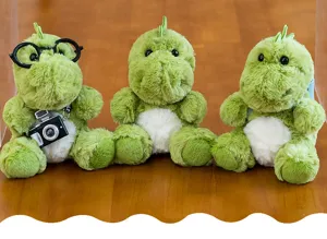 Detalle de tres lindos peluches de dragón verde con gafas y accesorios de cámara.
