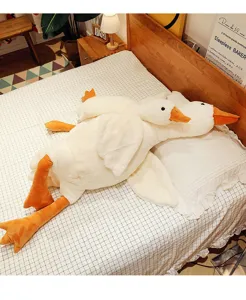 Grandi e piccoli cuscini di peluche a forma di oca bianca su una comoda superficie del letto