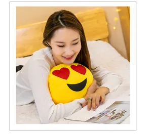 Young woman resting with a heart-eyed emoji plush pillow while reading a magazine.