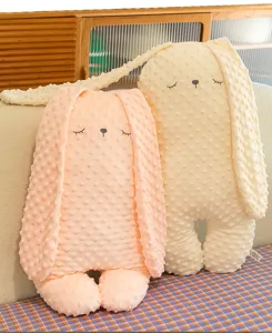 Dettaglio ravvicinato di morbidi cuscini a coniglio in peluche rosa e color crema