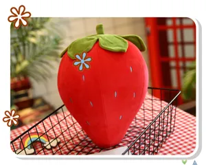 Grande cuscino di peluche a forma di fragola rossa in un cesto di metallo nero su un tavolo.