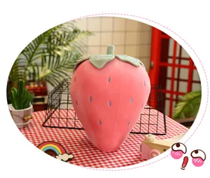 Cuscino di peluche a forma di fragola con dettagli di foglie verdi e punti rossi.