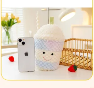Peluche colorato a forma di tazza con sorriso accanto a uno smartphone per le dimensioni.