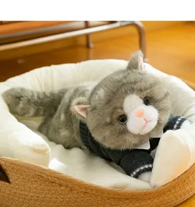 Close-up of a realistic plush gray cat wearing a black sweater in a cat bed
