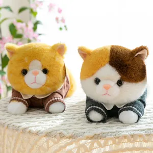Two cute chubby plush cats wearing sweaters lying on a cozy white knitted surface