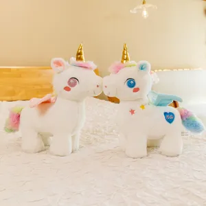 Due simpatici peluche di unicorno bianco con corna dorate e criniere arcobaleno su un letto