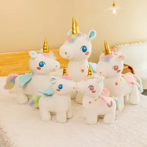 Set di cinque peluche unicorno bianchi con corna dorate e criniera arcobaleno su un letto