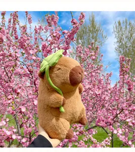 Primo piano di un simpatico peluche di capibara con foglia verde tra i fiori rosa accesi