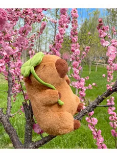 Simpatico peluche capibara con foglia verde seduto su un ramo di ciliegio rosa fiorito