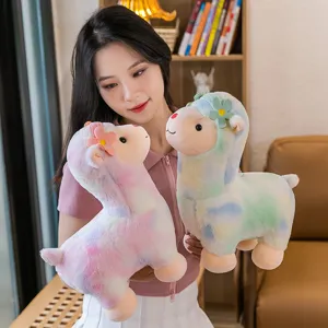 Cute rainbow alpaca plush toy dolls held by a model in a warm indoor setting