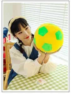 Detail view of a soft yellow and green plush soccer ball pillow held by a model.