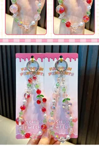 Close-up of colorful cherry beaded phone charms with sparkling rhinestones on cards. (90 chars)