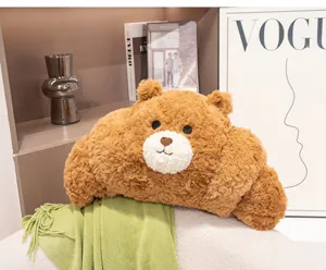 Detalle de un cojín de peluche con forma de oso croissant marrón en un ambiente hogareño.