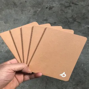Hand holding a set of A5 kraft paper notebooks with stitched binding and minimalist white logo