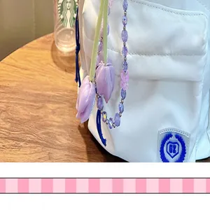 White fabric bag detail with purple tulip beaded charm pendant, stylish bag accessory strap for use.