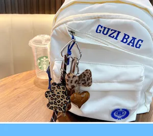 Detailed close-up of plush leopard print bear and heart keychain set on a white backpack