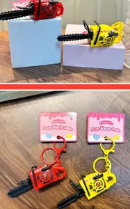 Mini vibrating chainsaw keychain toy with cute pull-string design in red and yellow.