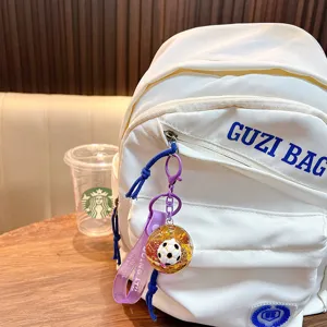 Soccer ball liquid glitter keychain with purple strap hanging on a white backpack