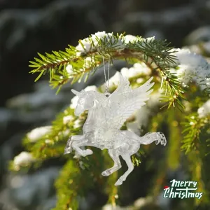 Detailed view of a transparent acrylic Pegasus hanging on a snowy Christmas tree branch.