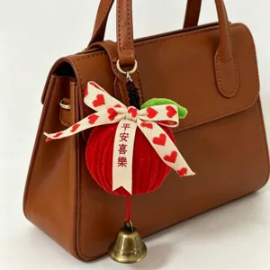 Detail view of red plush apple charm with heart bow and bell attached to a bag