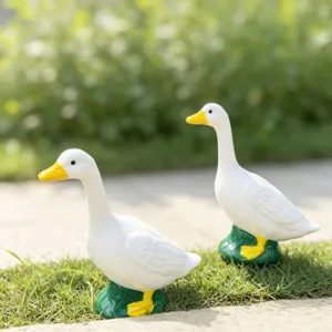 Primer plano de dos estatuas de gansos blancos de pie sobre hierba para decorar jardines