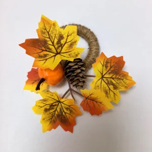 Detail of Thanksgiving napkin ring with orange pumpkin, yellow maple leaves and pinecone