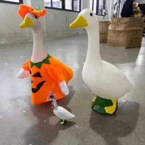 Detail view of large white goose garden statues with festive Halloween pumpkin outfit
