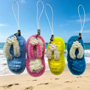 Detail view of handmade flip-flop keychains with pearl flowers on a sunny sandy beach