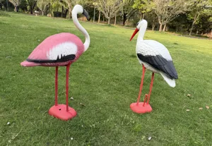 Lifelike plastic flamingo and stork garden ornaments standing on green lawn