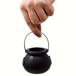 Hand holding a small black Halloween witch cauldron prop for candy