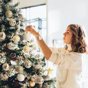 Close-up of a woman decorating a snowy Christmas tree with gold and white baubles.