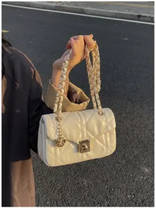 Detail view of a luxury beige quilted crossbody bag with gold chain strap and rose charm.