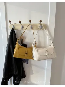 Detail view of vintage oil wax leather underarm bags with buckle pockets on a coat rack