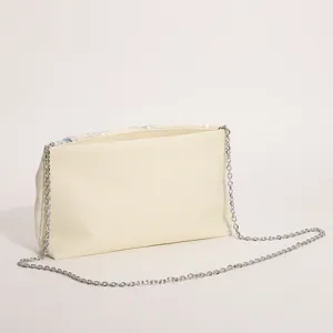 Vista dettagliata della borsa a tracolla in tessuto beige da donna con catena e decori.