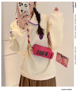 Detail of a retro fuchsia brick phone shaped crossbody bag worn by a model in soft light.