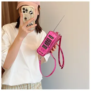 Close-up of a creative bright pink brick-phone shaped crossbody bag held by a model