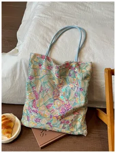 Detail of a chic sequin tote bag featuring colorful geometric embroidery and blue straps.