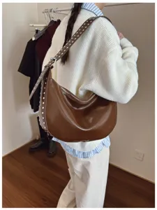 Detailed shot of a brown rivet hobo bag worn by a model, showing texture and strap design.
