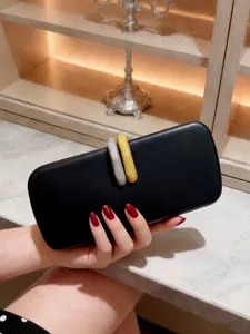 Elegante pochette da sera nera con chiusure gialle e grigie tenuta in mano con cura.