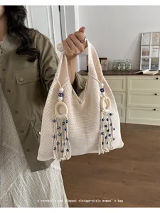 Lifestyle-Aufnahme einer beigen Stricktasche mit Quasten und Holzringen.