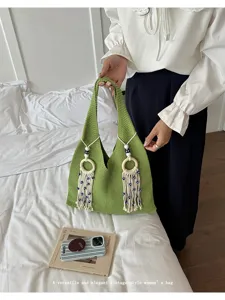 Detail einer grünen Stricktasche mit weißen Quasten und dekorativen Perlen auf weißem Bett