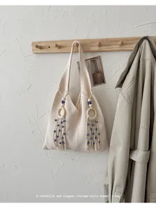 Minimalistische cremefarbene Stricktasche mit eleganten Quasten und Holzring-Details.